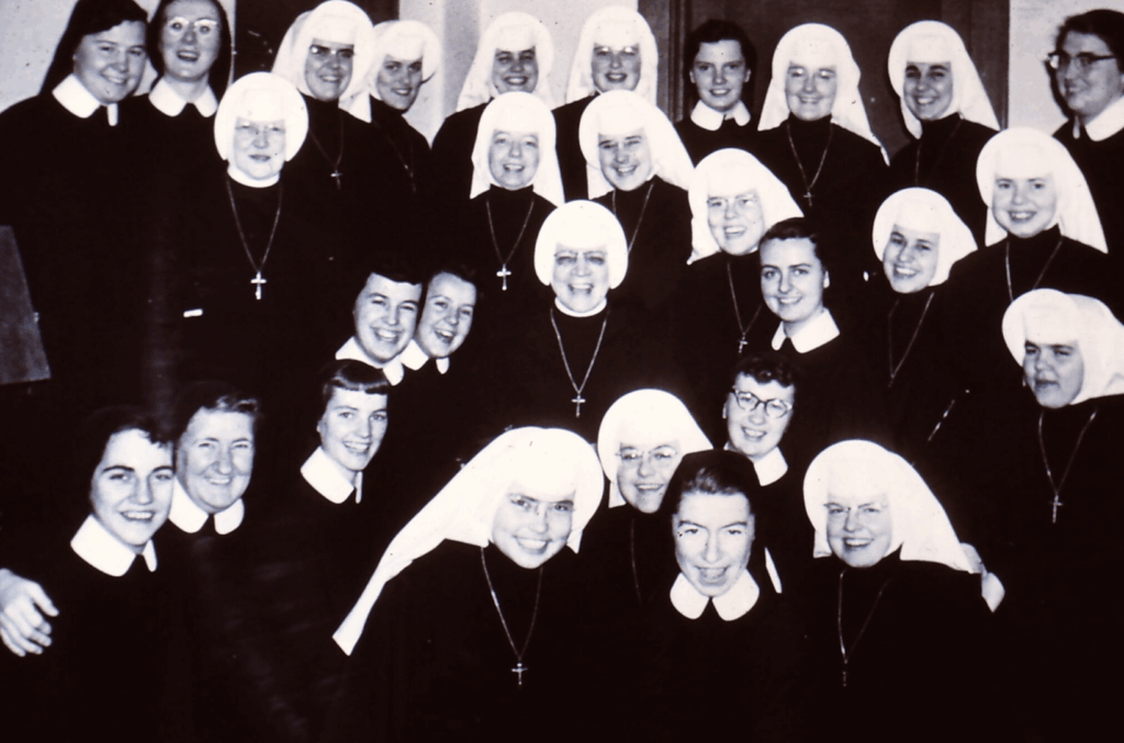 about 25 nuns with white and black veils smiling