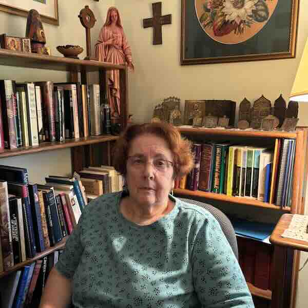 Sandra Miesel sitting in a chair in her home, surrounded by books.