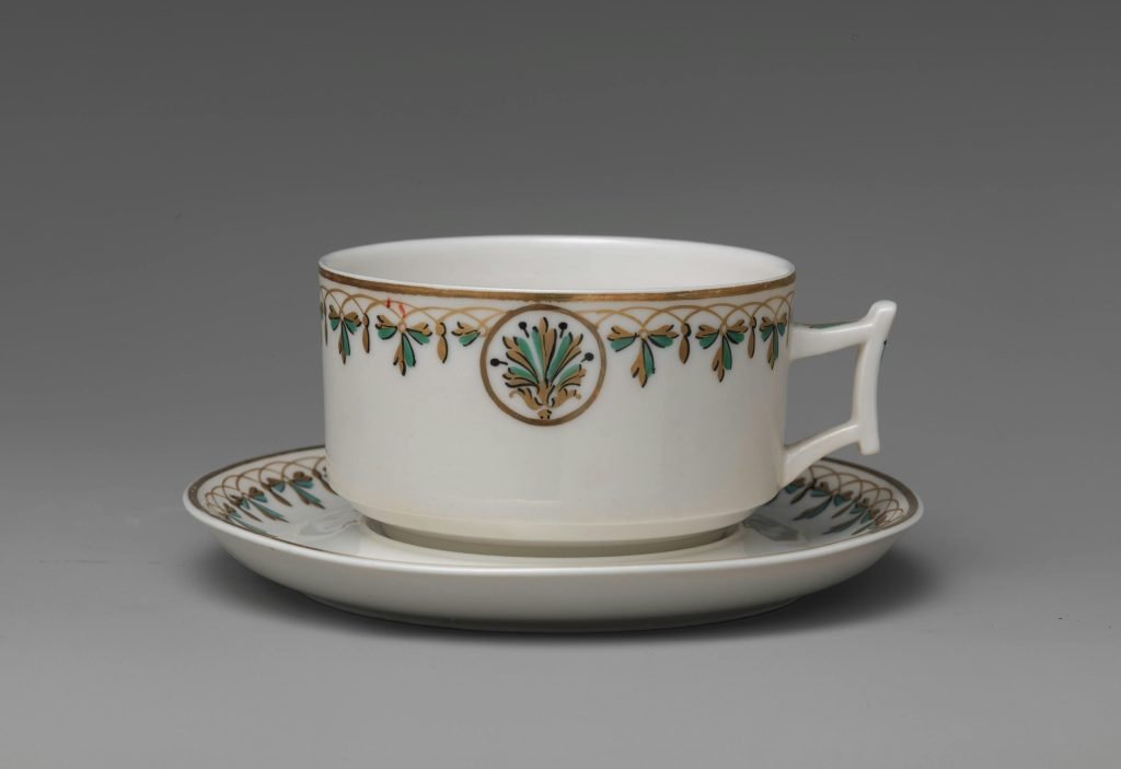 an antique coffee cup with ornate etching on edge with saucer