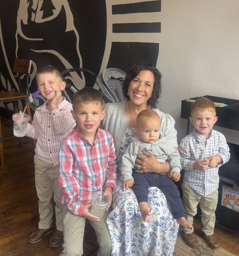 a seated woman with dark hair poses with four small boys