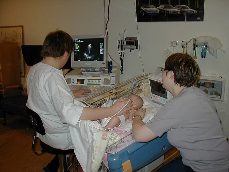 A sonographer completes a test on a baby with a mother hovering nearby