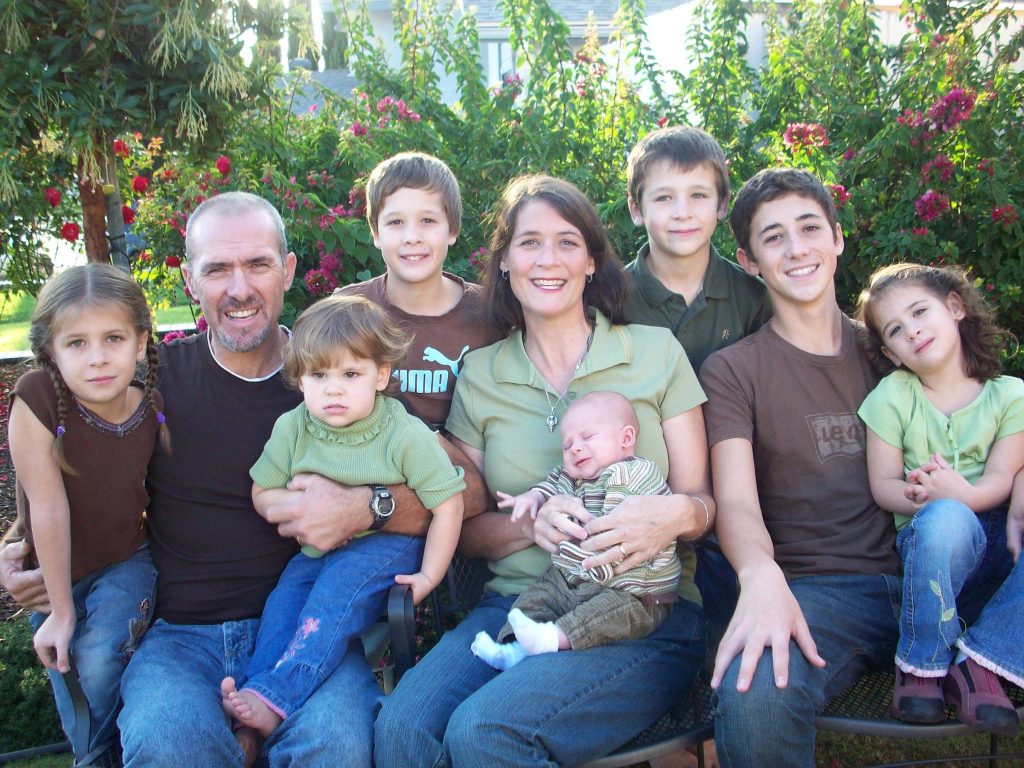 A family with seven kids in a garden wearing green and brown shirts