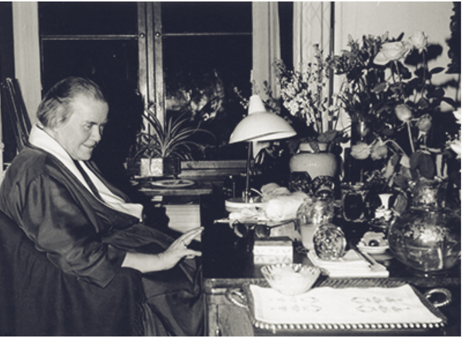 An older woman at a desk with flowers and books