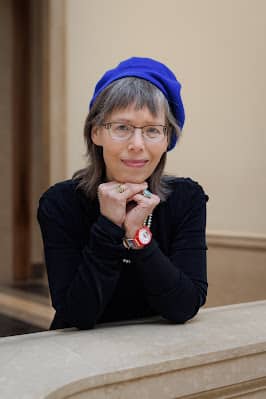 A woman in a blue beret is kneeling and smiling at the camera