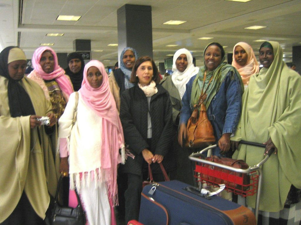 Image of woman of different nationalities in a group photo at an airport with their luggage.